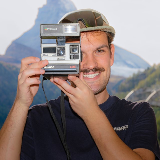 Nuno Fernandes smiling behind a Polaroid camera, the Matterhorn behind him